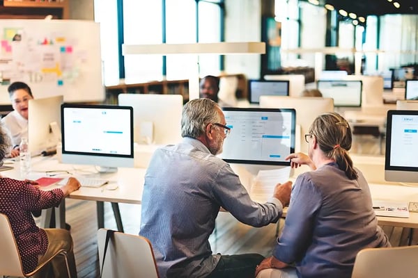 Two CCDI colleagues in an open concept office reviewing cybersecurity measures on a computer, with a vector graphic depicting a cloud and shield representing cybersecurity